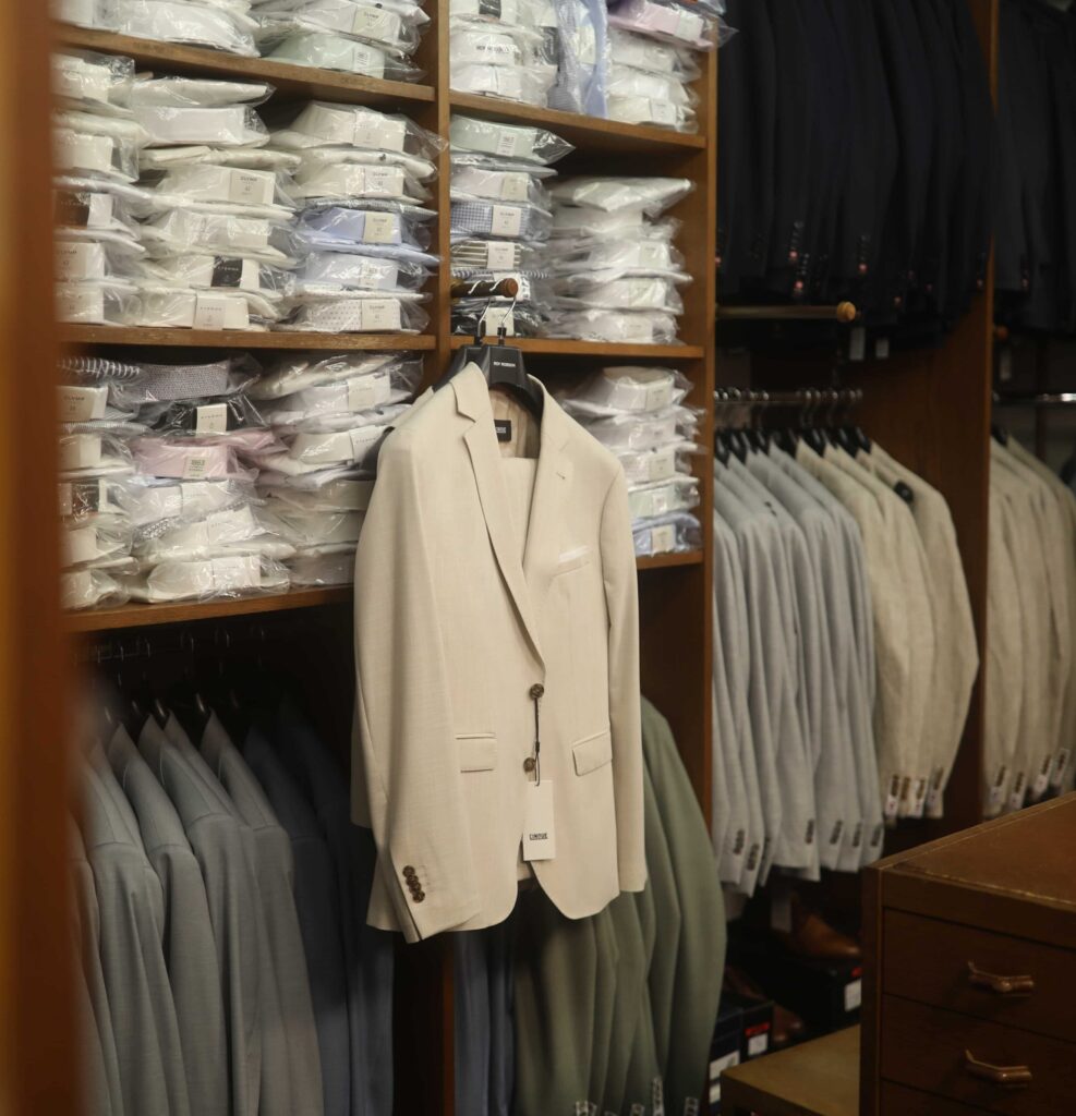 Hochzeitsanzüge hängen auf Kleiderhaken im Geschäft, im Fokus eine weiße Anzugsjacke