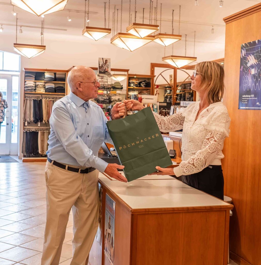 Übergabe der Einkaufstüte einer Mitarbeiterin an einen Kunden bei Herrenmode Pöchhacker