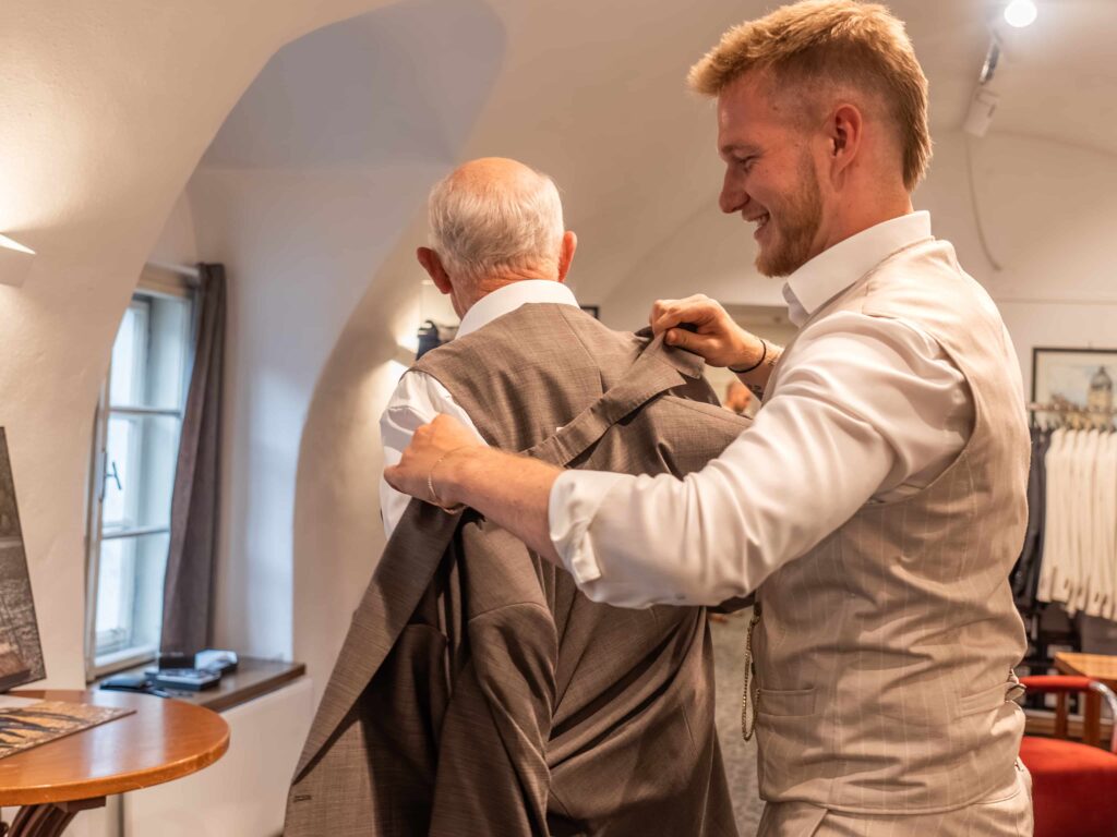 junger Mitarbeiter hilft älterem Herren bei der Anprobe seiner Anzugsjacke