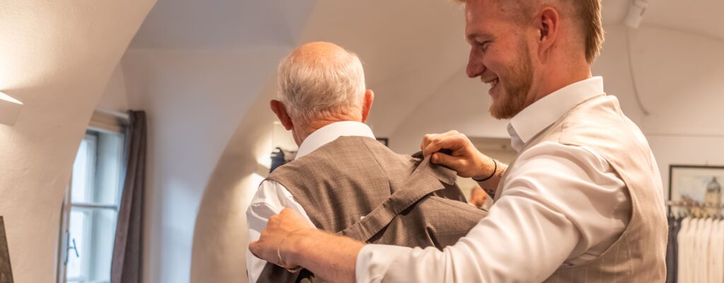 junger Mann hilft älterem Herren bei der Ankleide von einem Anzug