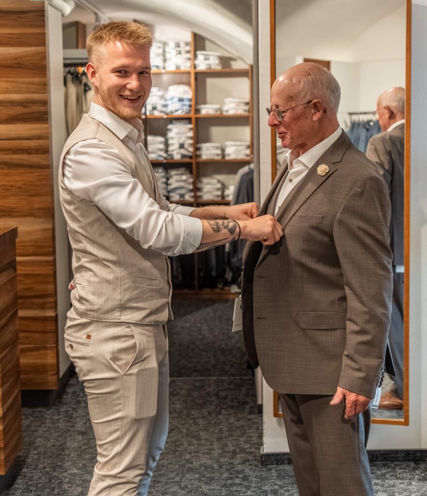 junger Mann hilft älterem Herr bei der Anprobe eines Anzugs
