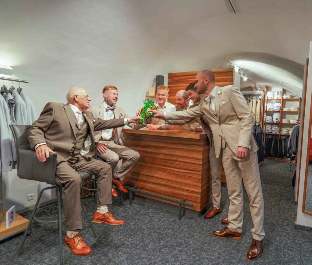 sechs Männer im Anzug stoßen auf ihre gekauften Hochzeitsanzüge an