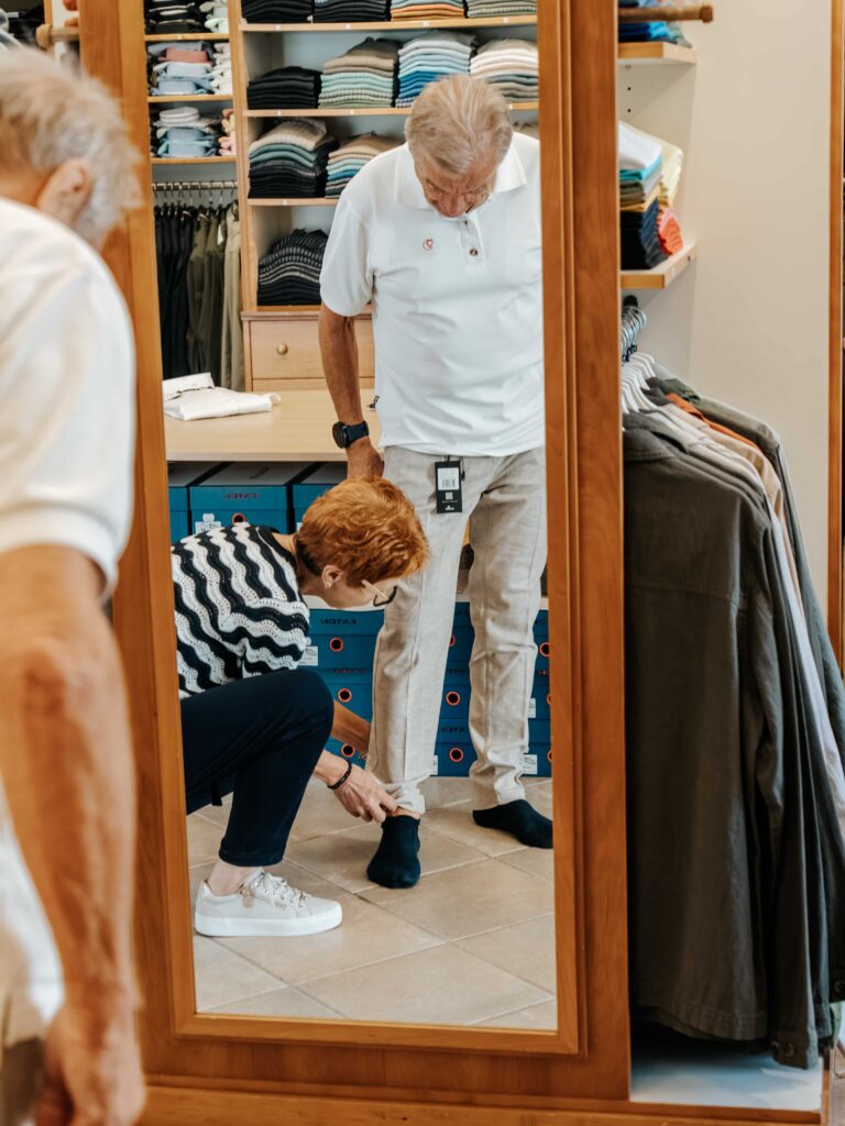 Mitarbeiterin hilft älterem Herren bei der Anprobe